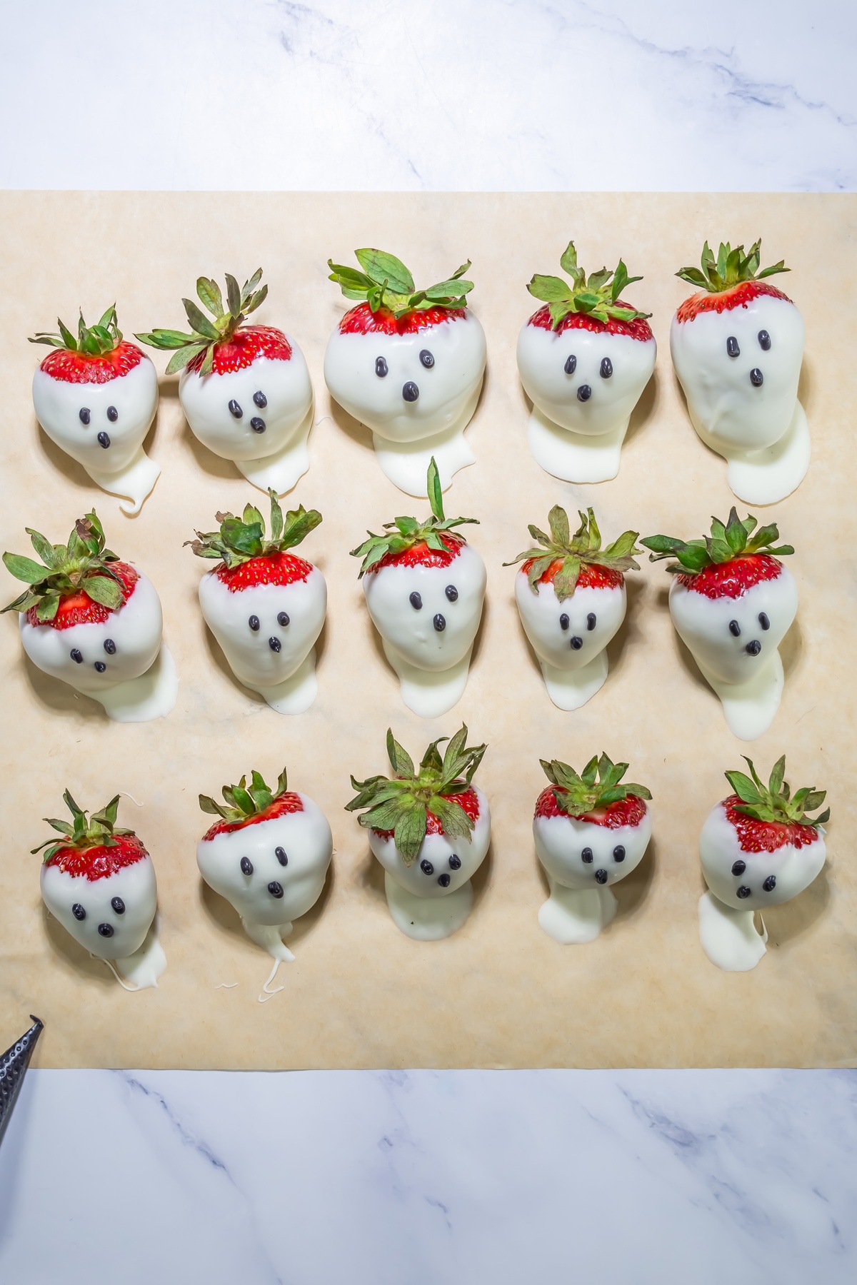 Strawberries dipped in white chocolate with chocolate chip faces arranged in rows on parchment paper to look like ghosts.