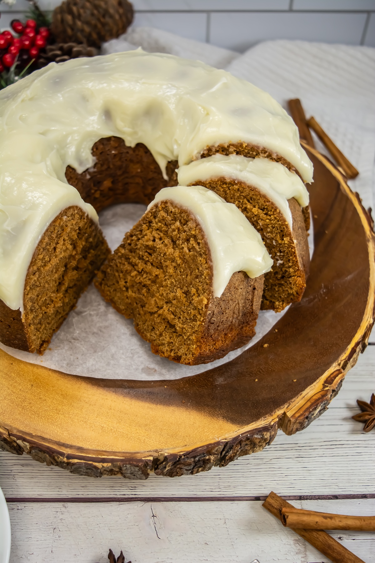Gingerbread bundt cake with cream cheese frosting on a rustic wood slice, with two slices cut.
