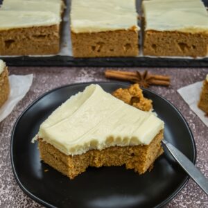 A slice of gingerbread sheet cake with cream cheese frosting on a black plate.