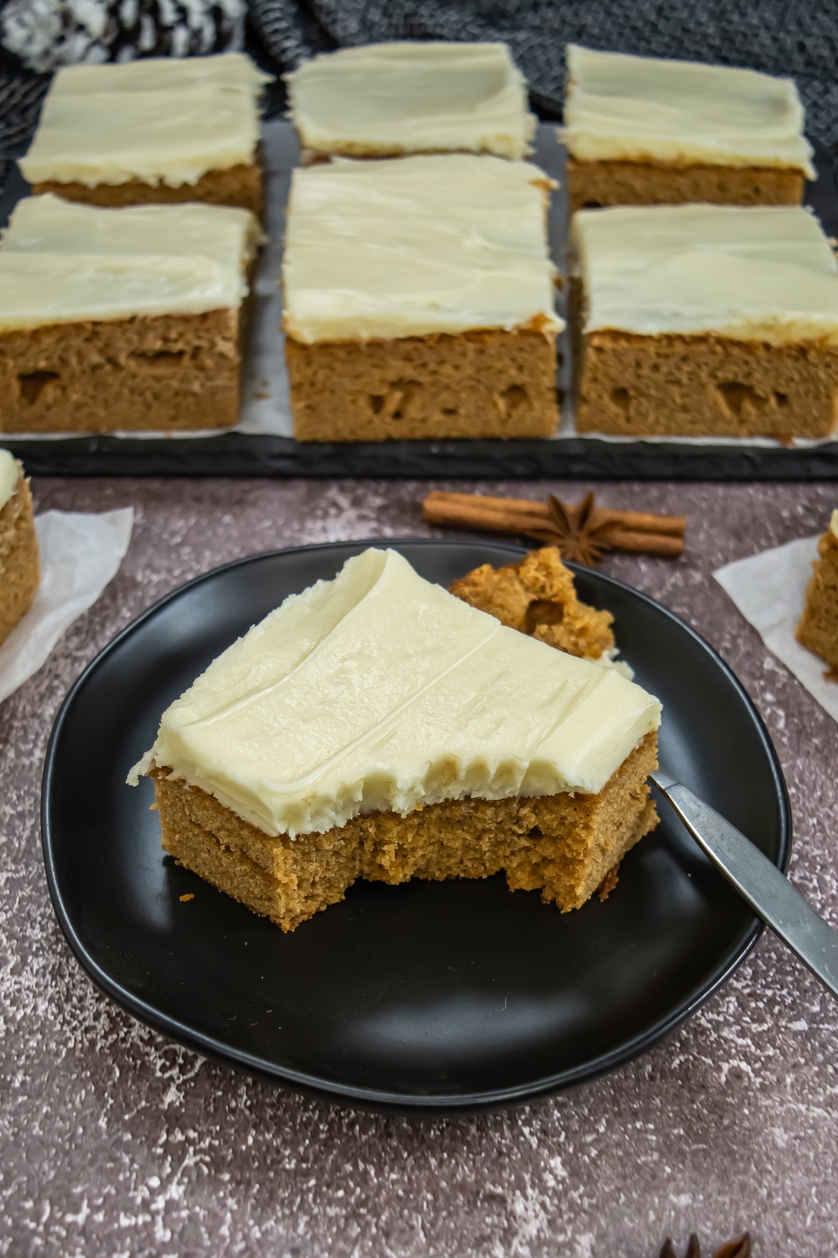 A slice of gingerbread sheet cake with cream cheese frosting on a black plate.