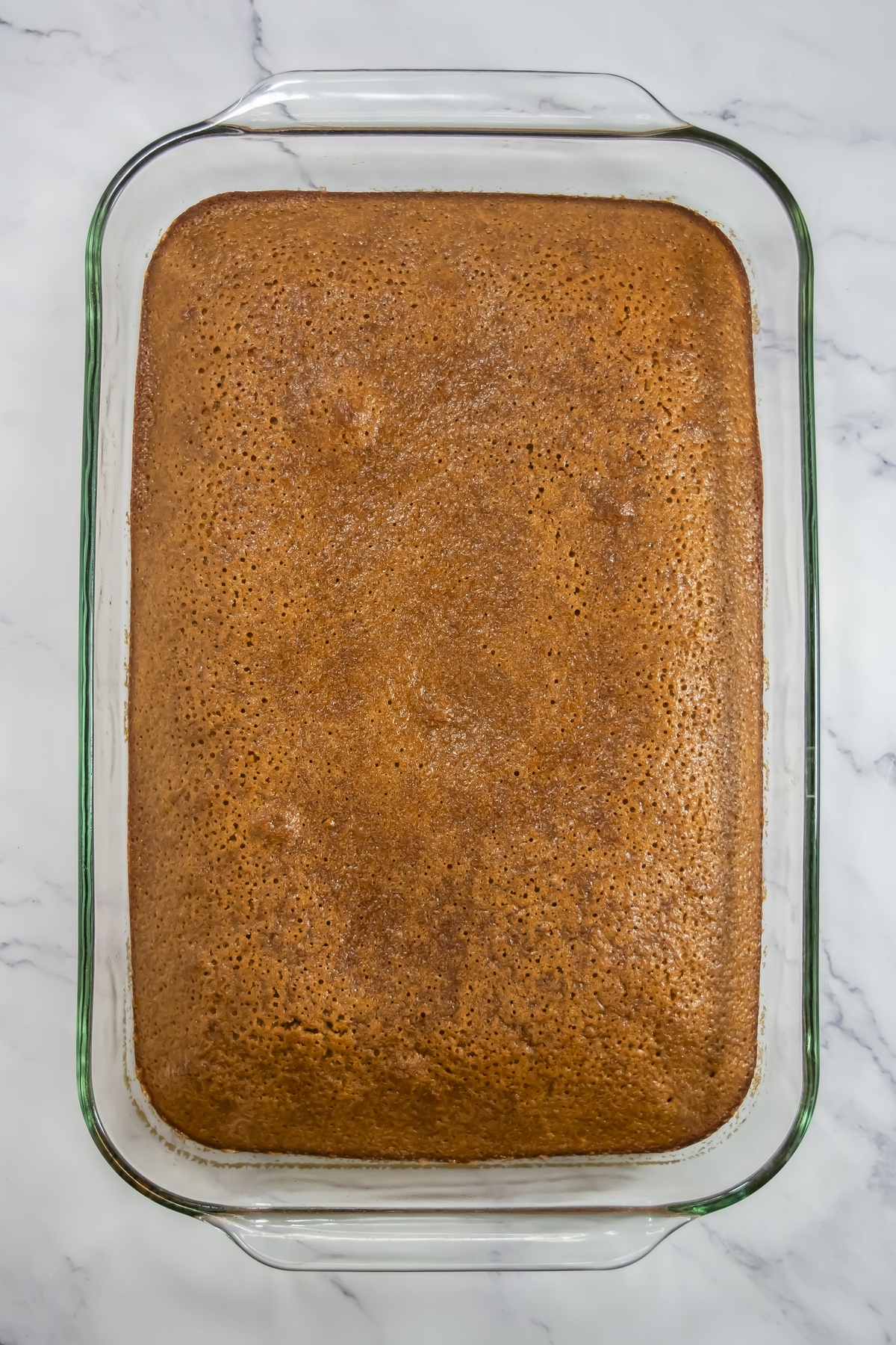 Freshly baked gingerbread cake with a golden-brown top in a rectangular glass baking dish on a marble surface.