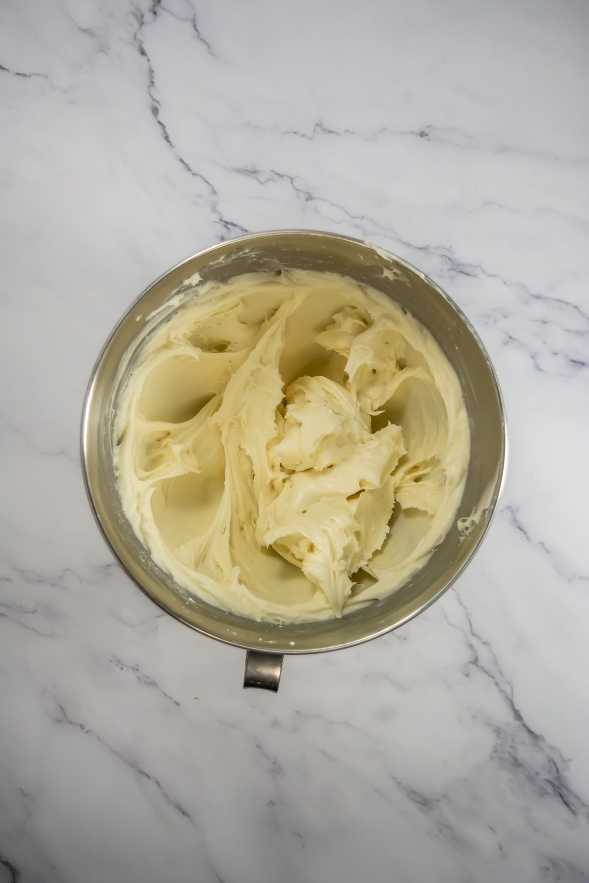 Creamy pale yellow frosting whipped smooth in a stainless steel mixing bowl on marble surface.