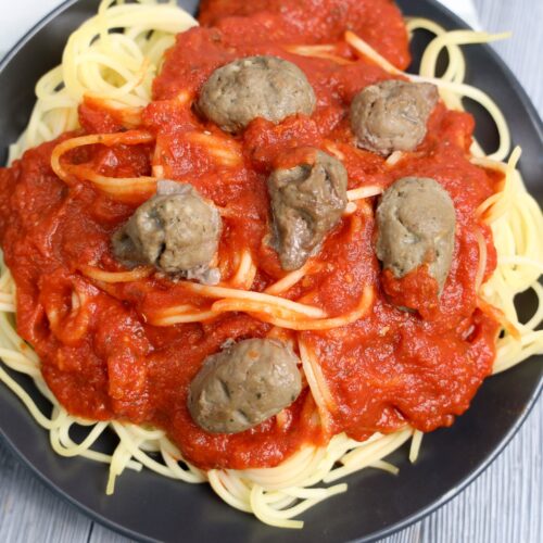 Halloween Spaghetti topped with red tomato sauce and meatballs served on a dark plate.