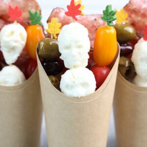 Halloween Charcuterie cups with mozzarella balls, olives, cherry tomatoes, mini peppers, and cured meat on skewers.