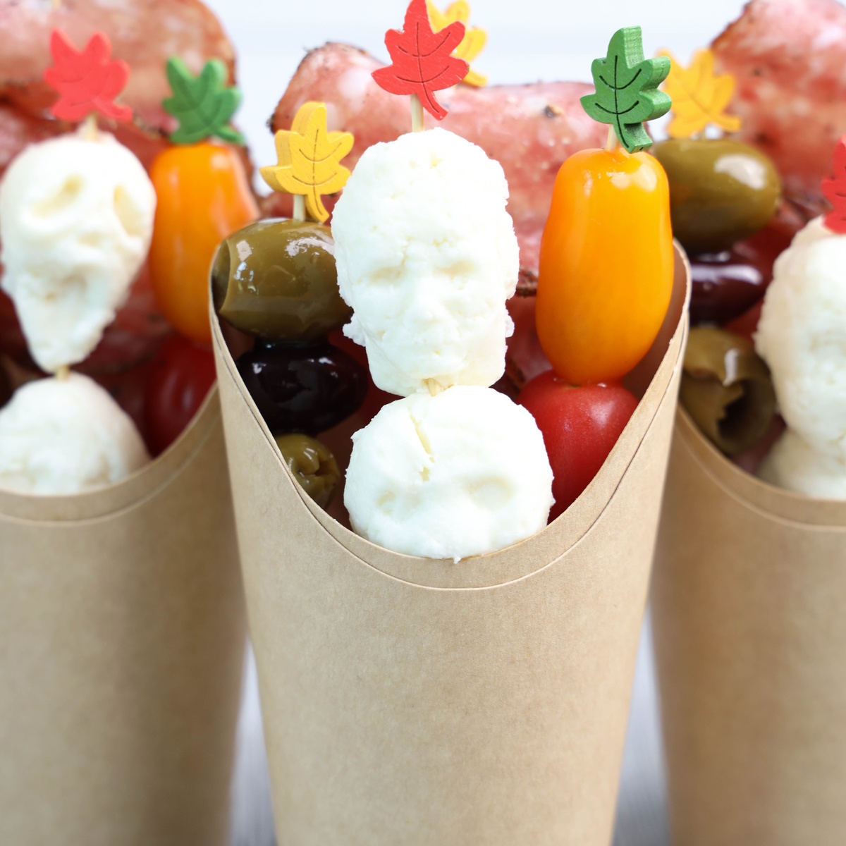 Halloween Charcuterie cups with mozzarella balls, olives, cherry tomatoes, mini peppers, and cured meat on skewers.
