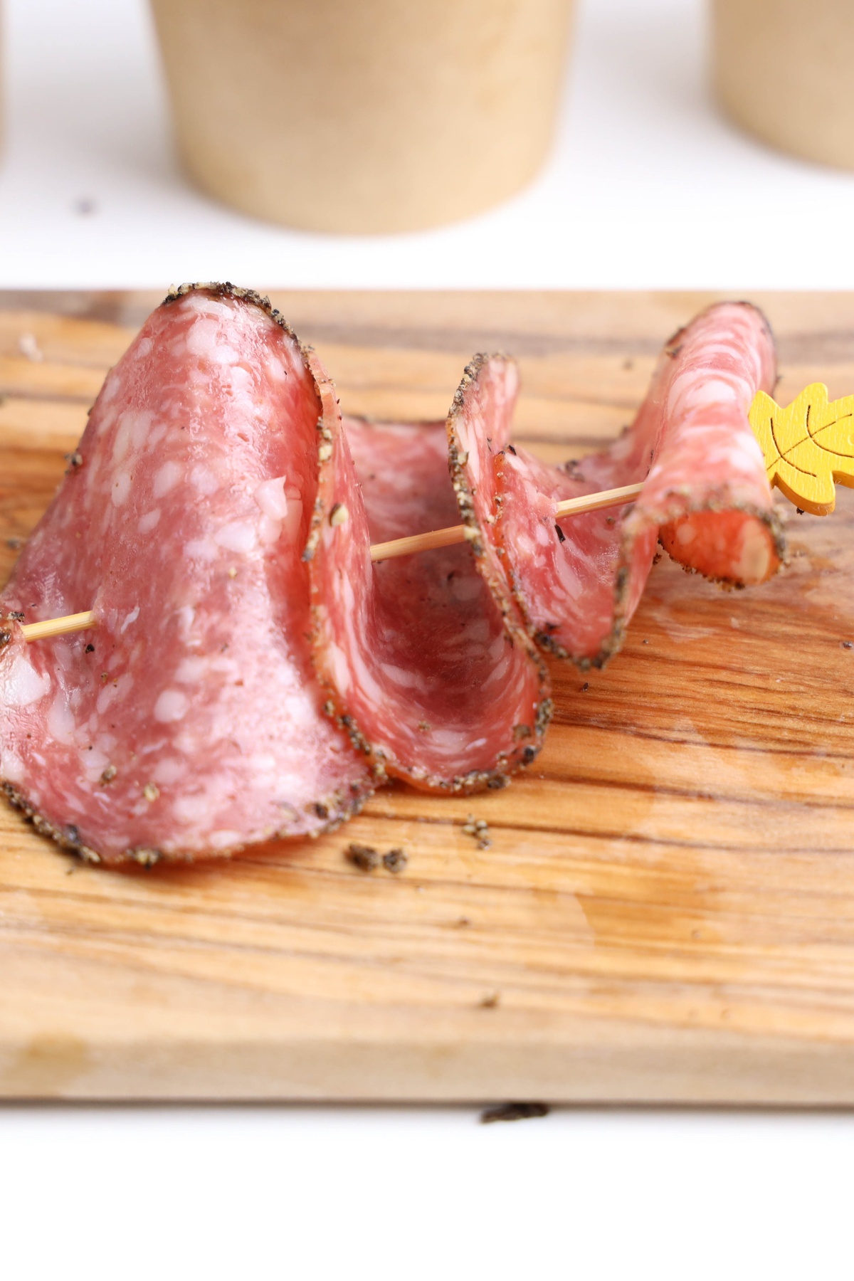 Sliced peppered salami folded and threaded onto a wooden skewer with yellow leaf decoration on a wooden cutting board.