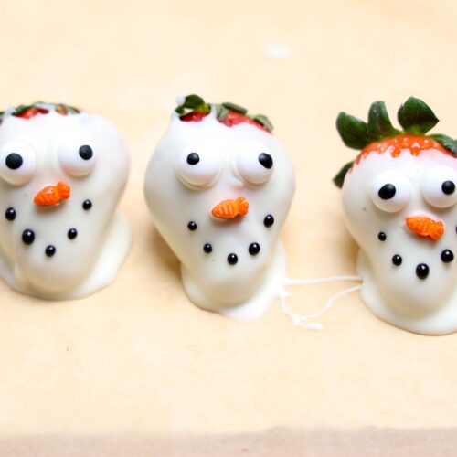 Melted snowman decorated strawberries on parchment paper.
