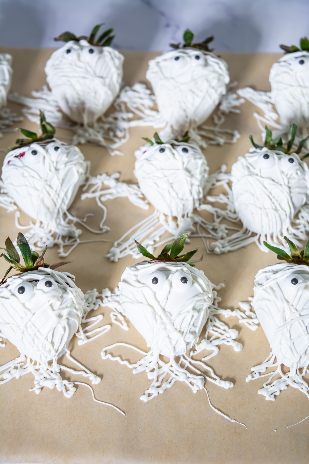 Strawberries dipped in white chocolate with drizzled white chocolate "bandages" and candy eyes arranged on parchment paper.
