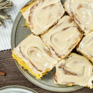 Pumpkin cinnamon rolls with cream cheese frosting arranged on a gray plate.