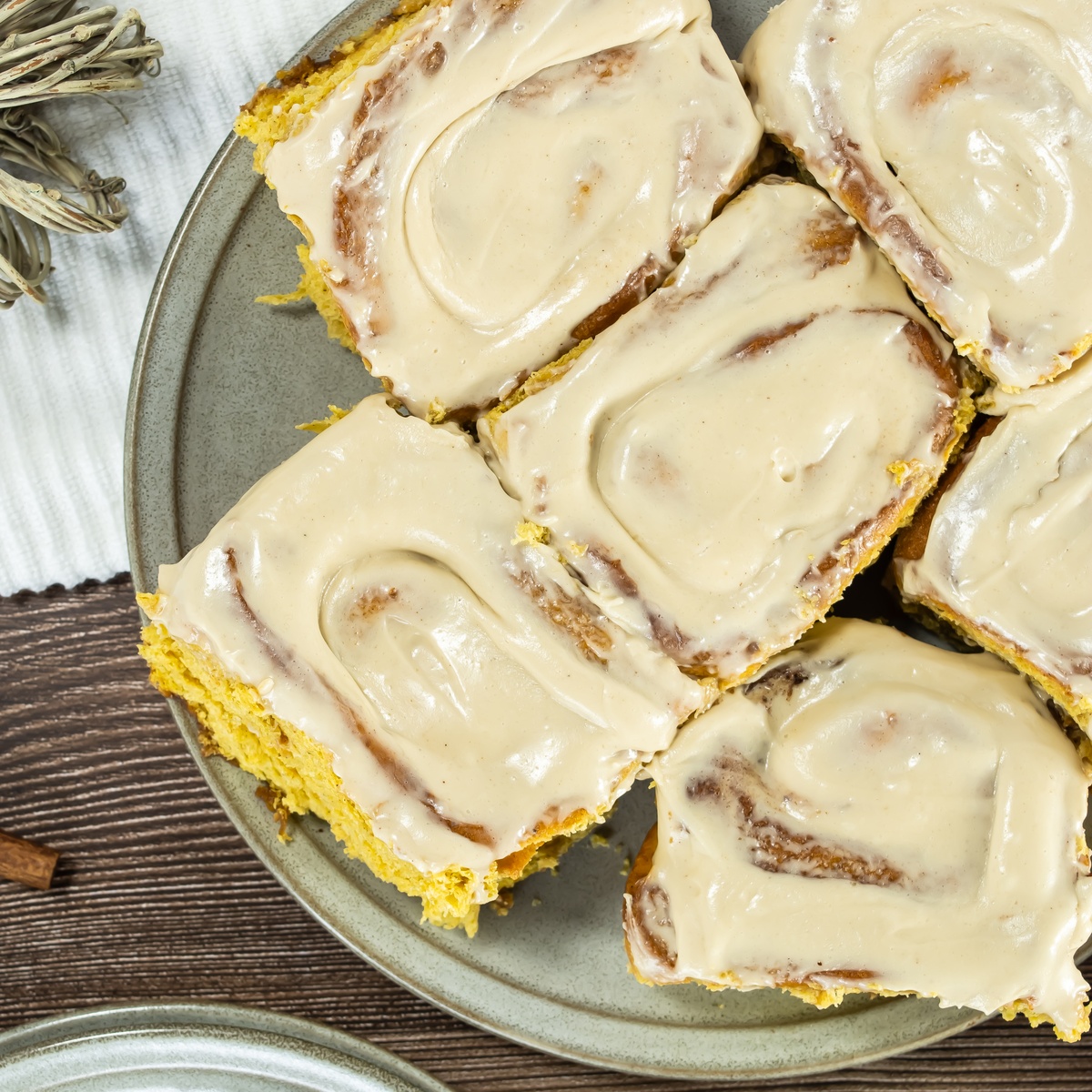 Pumpkin cinnamon rolls with cream cheese frosting arranged on a gray plate.