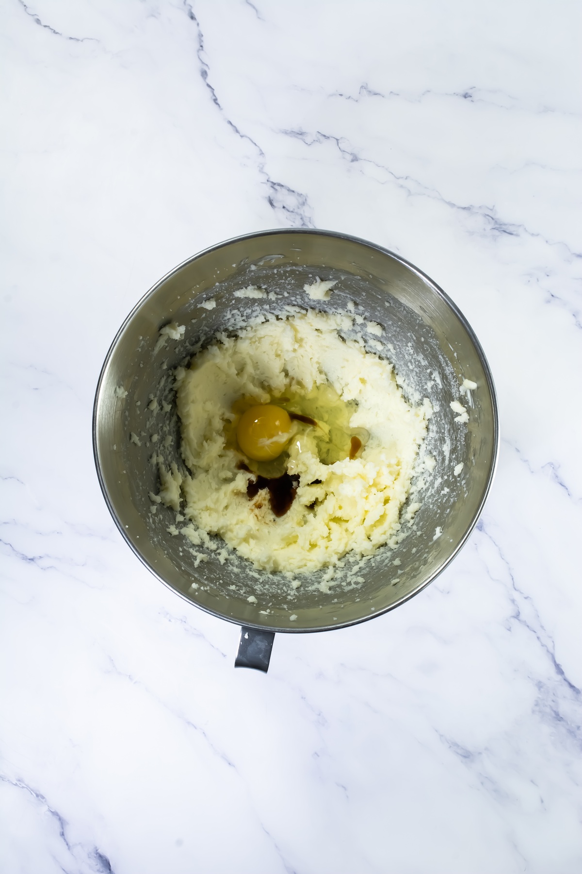 Stainless steel mixing bowl with creamed butter and sugar, a raw egg,.