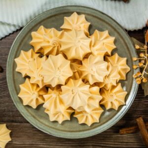 A green ceramic plate filled with golden star-shaped pumpkin meringue cookies.