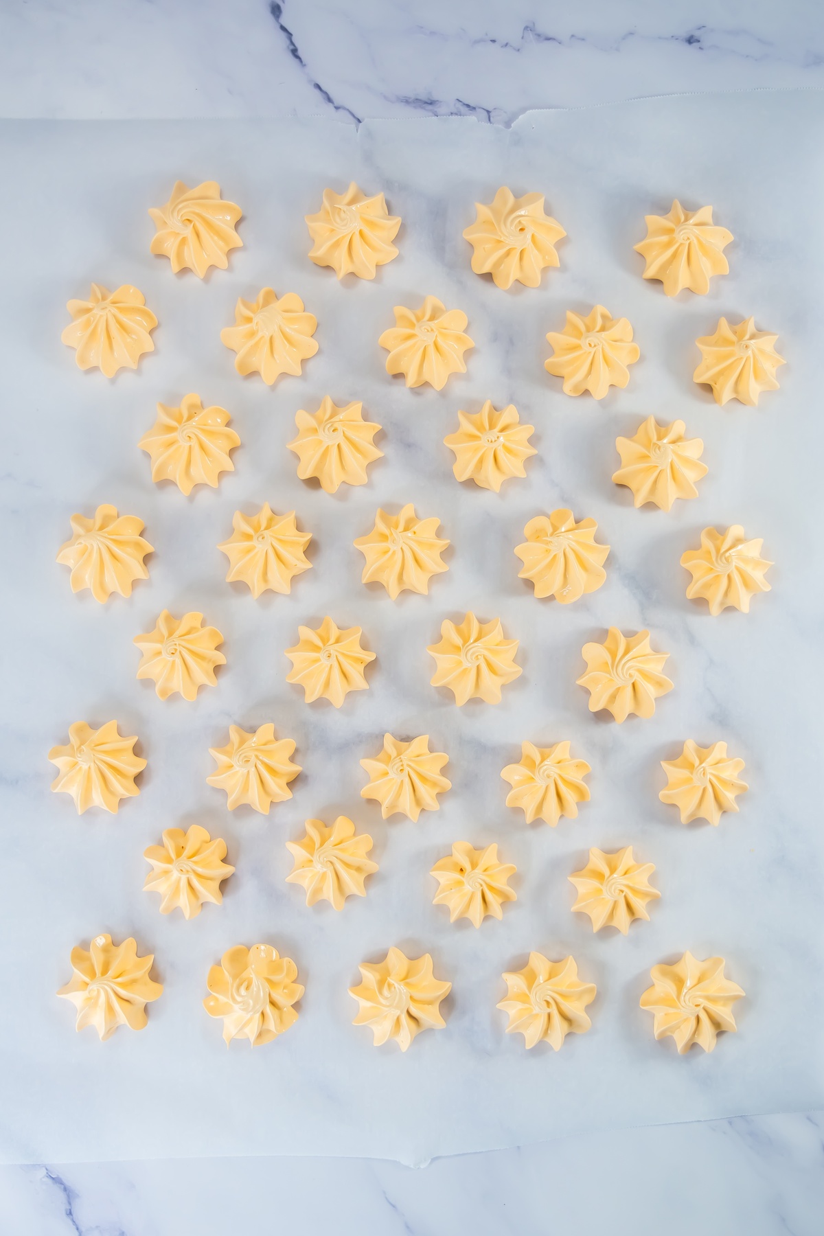 Piped orange-tinted meringue cookies in swirled rosette shapes arranged on parchment paper before baking.