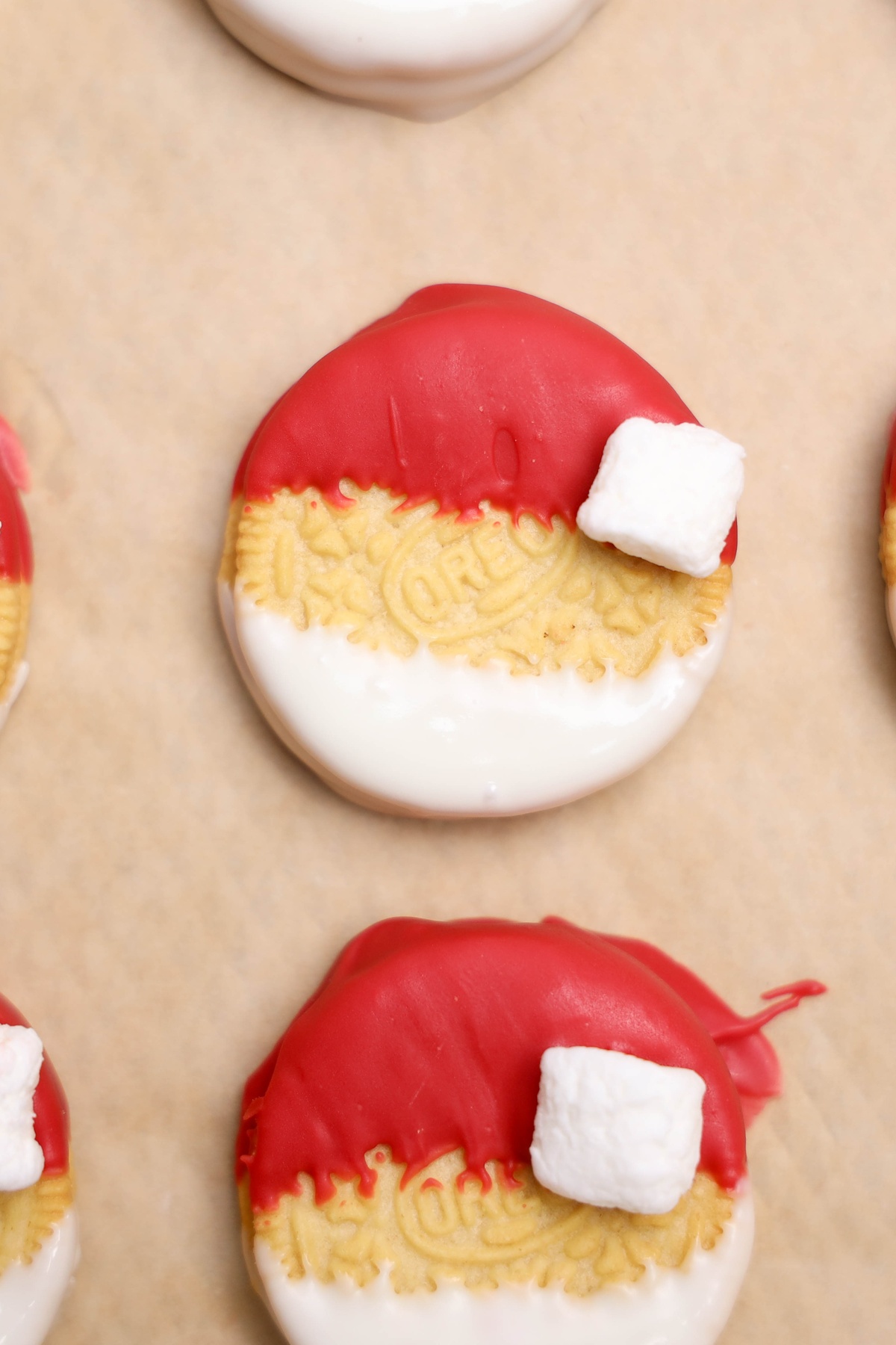 Golden Oreo cookies decorated as Santa hats with red candy coating on top.