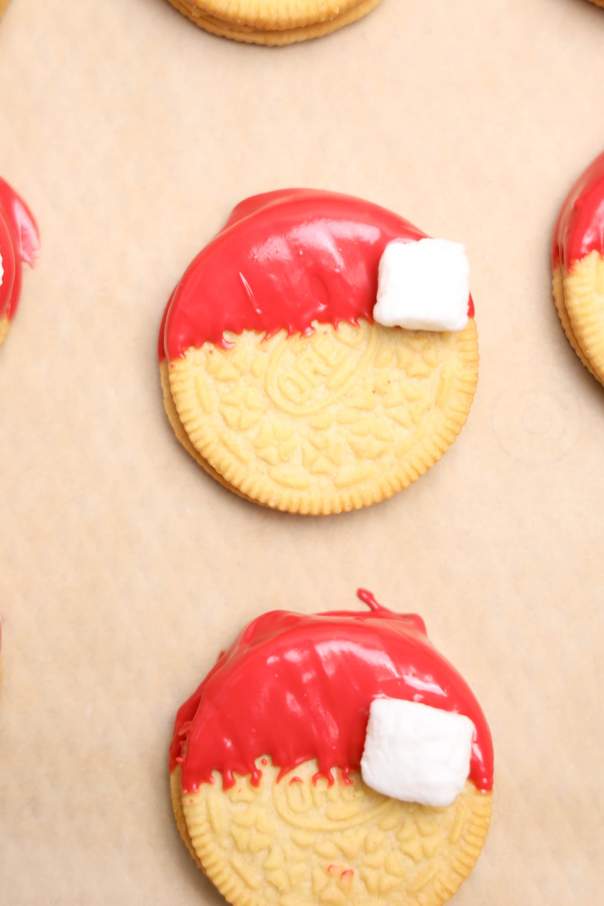 Golden Oreo cookies half-dipped in red candy coating with mini marshmallows attached, arranged on parchment paper.