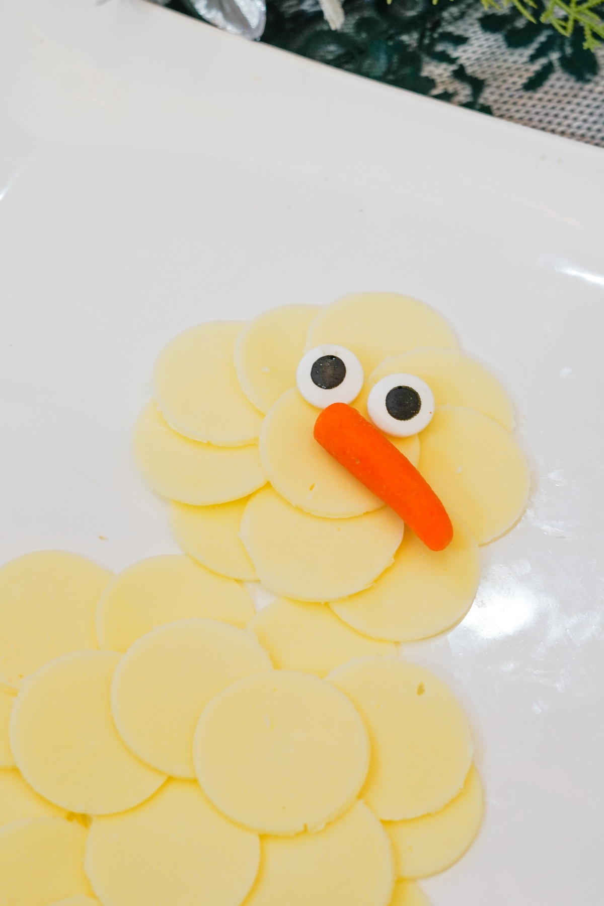 Round cheese slices arranged in a snowman shape on a white platter with candy eyes and a baby carrot nose.