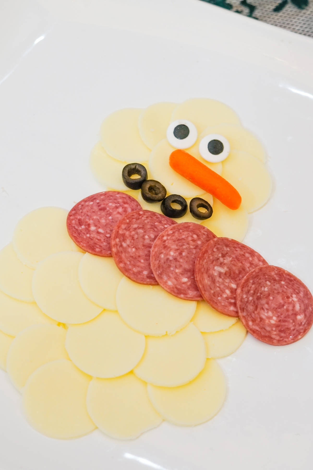 Snowman shape made from overlapping provolone cheese slices with candy eyes, carrot nose, olive slice mouth.