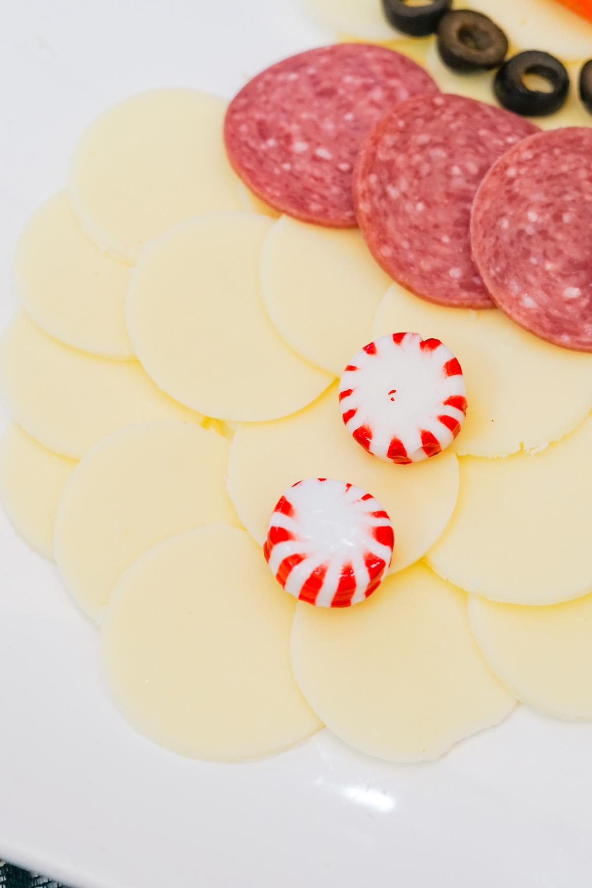 Snowman shape in progress with provolone cheese slices forming the body, salami slices and black olives at the top.