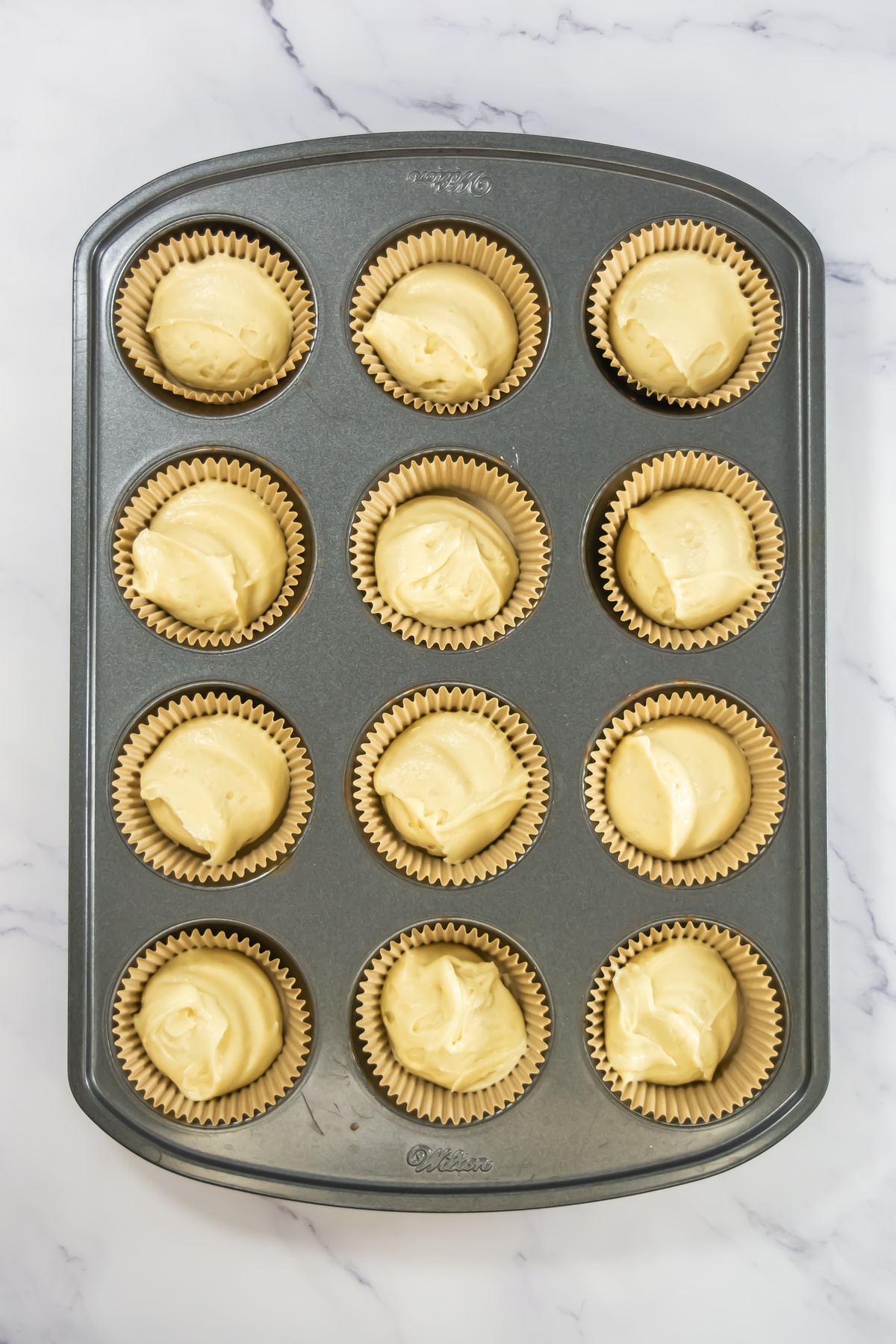 Cupcake batter in cupcake liners in a baking sheet.